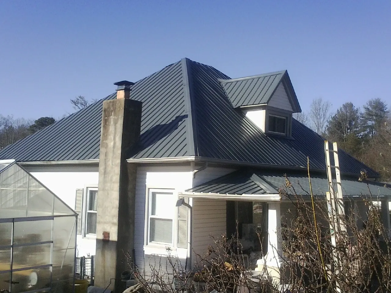 Dark blue standing seam metal roof on a white farmhouse with dormer — Slate & Tile Roof Repair by Roofing Brothers in Mount Olive