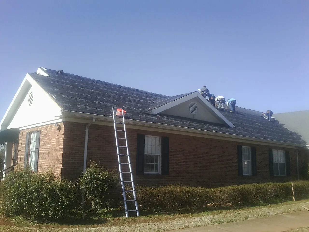 Crew tearing shingles off a brick ranch roof with a ladder set — Emergency Roof Repair work by our crew in Mount Olive