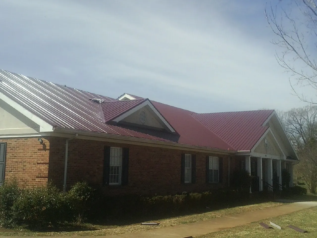 Red metal roof with gabled entries on a long brick building, from a Hail Damage Roof Repair job in Mount Olive