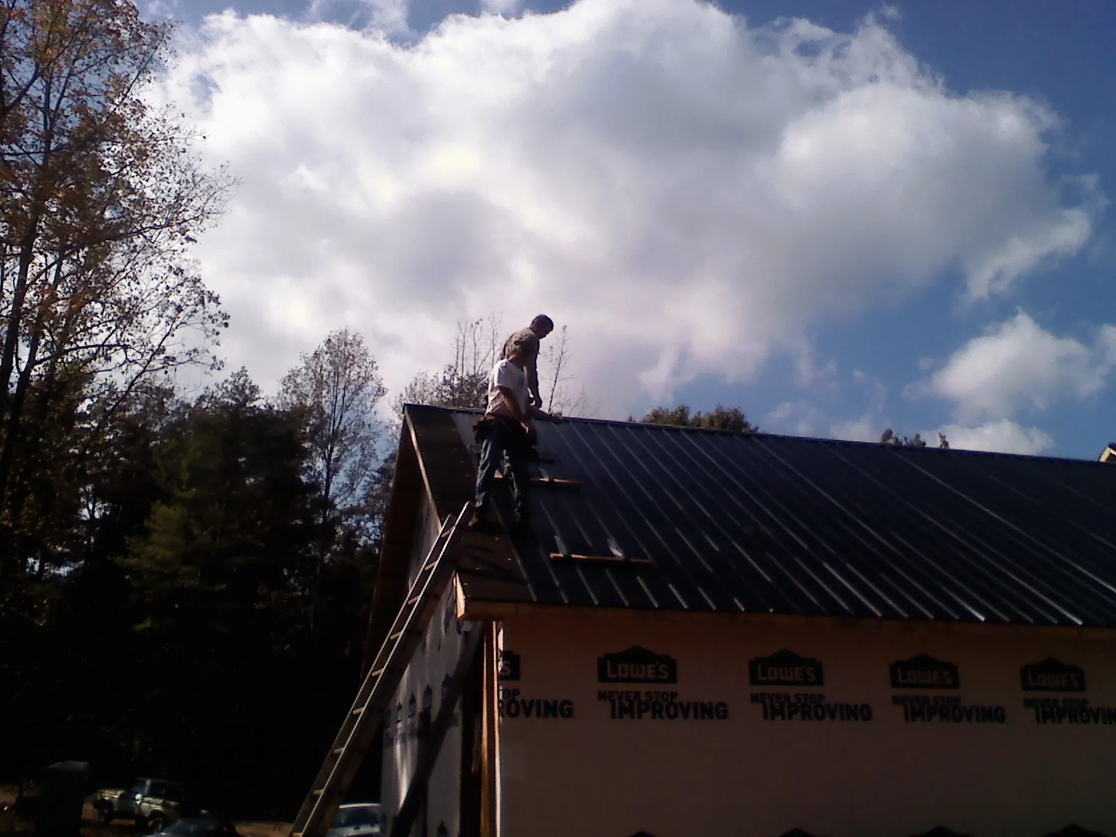 Roofer fastening dark metal panels high against a cloudy sky, from a Roof Inspection job in Mount Olive